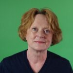 A headshot of Antonia Swinson, CEO at the Ethical Property Foundation with a green background, wearing a navy v neck jumper, red short hair.
